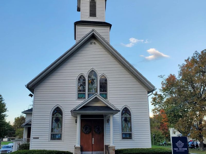 Front of the white church with steeple and red doors